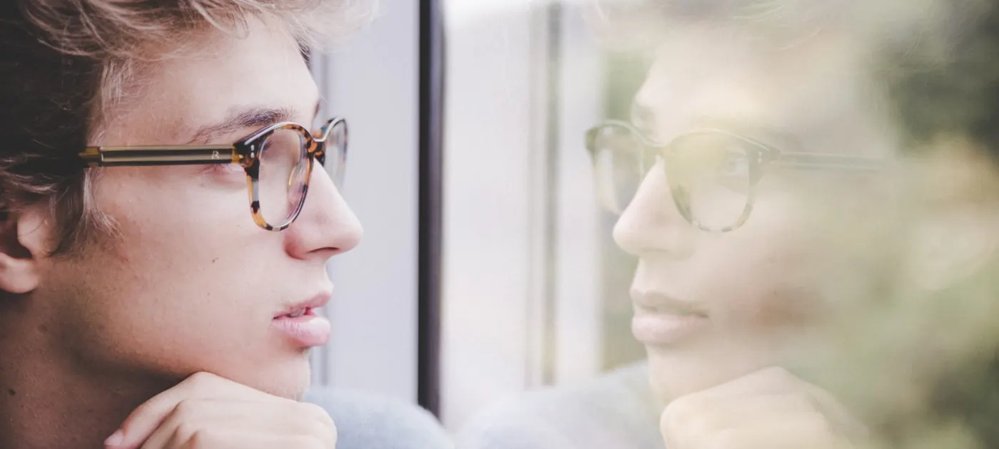a man wearing glasses looking out a window